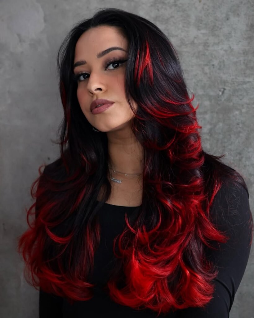 Woman with long, voluminous black hair featuring vibrant red highlights — a bold and edgy take on Fall Hair Colors.