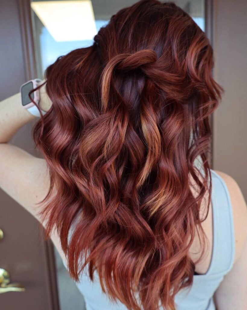 Back view of red copper hair styled in waves and a loose half-up twist — a vibrant and romantic Fall Hair Colors idea.

