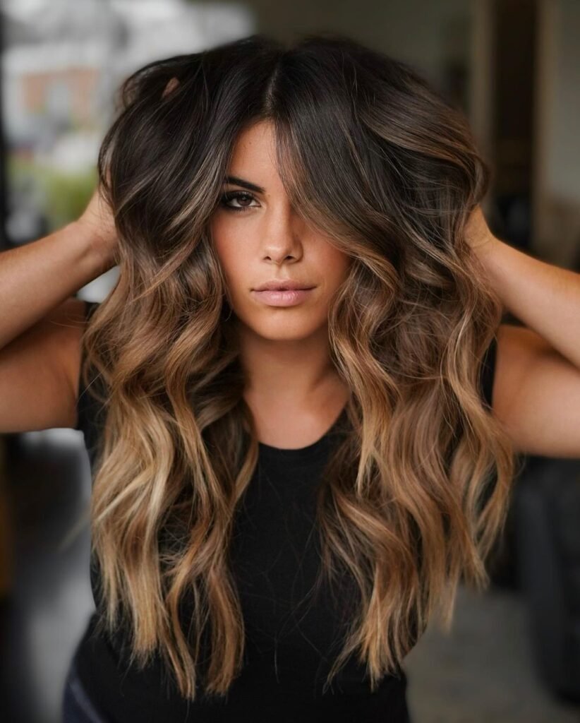 Woman with voluminous caramel balayage on dark brown hair — a sultry and textured Fall Hair Colors style.