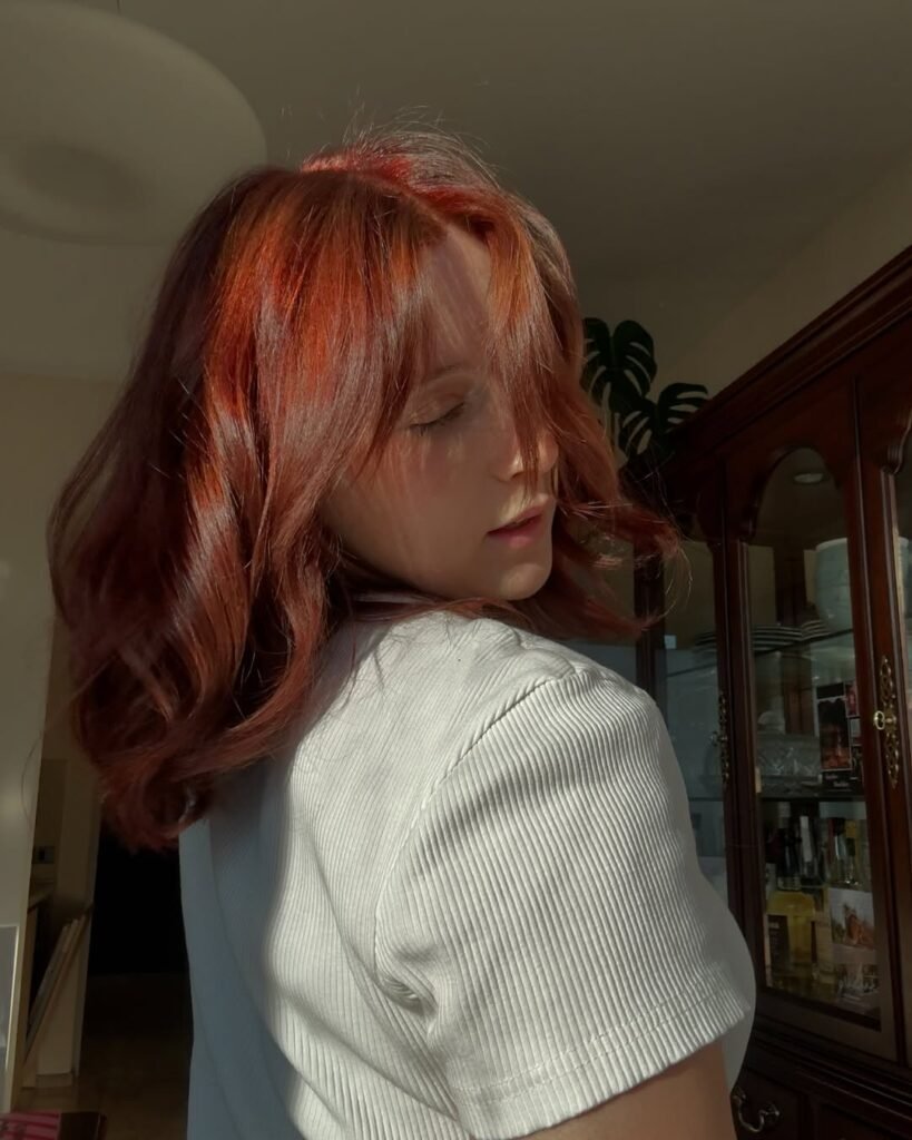 Woman with glowing red-orange highlights on shoulder-length hair — a fun and fiery Fall Hair Colors option.