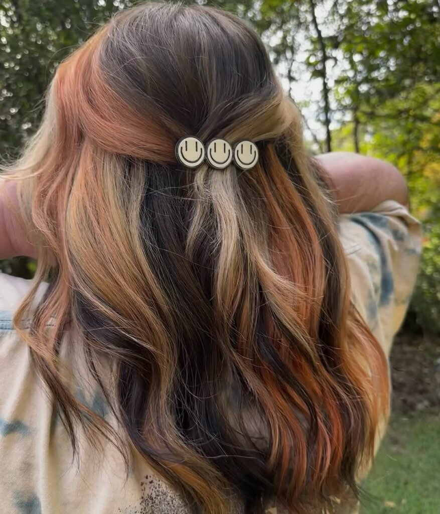 Back view of multi-toned pastel peach and brown hair clipped with smiley face pins — a playful and quirky Fall Hair Colors style.