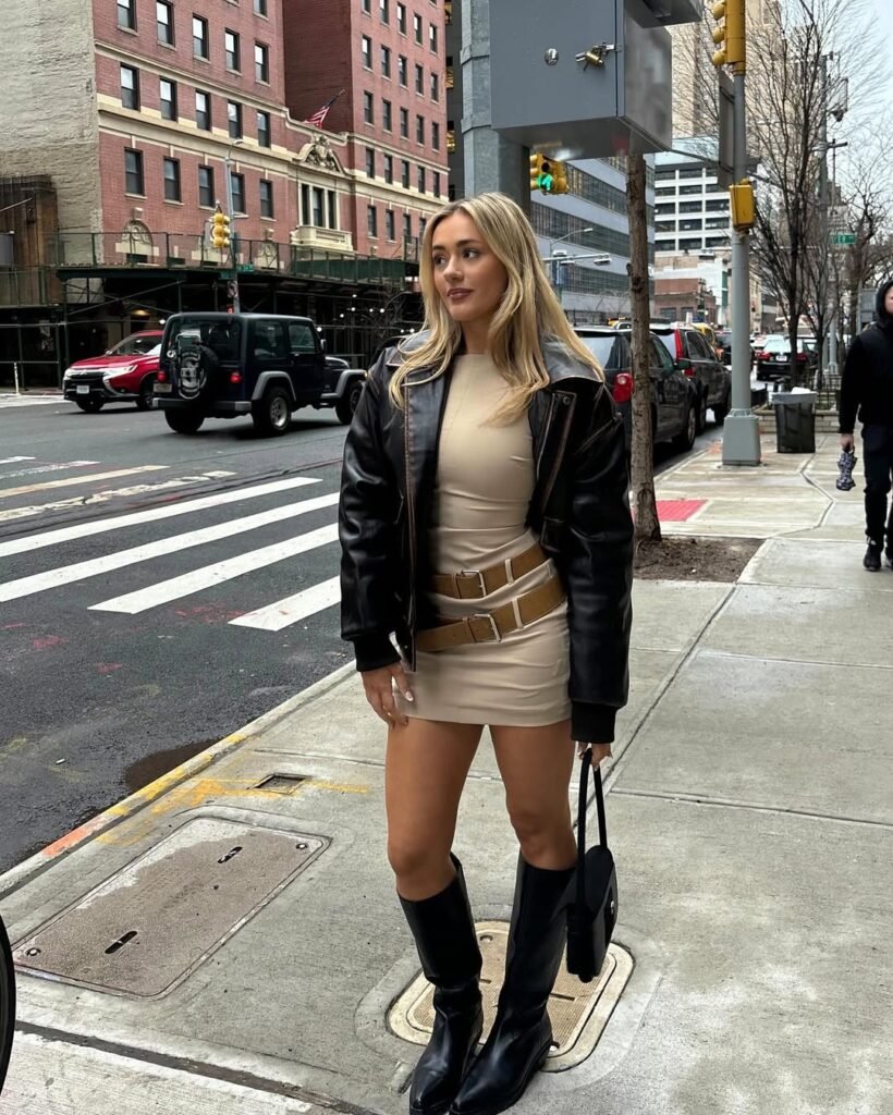 Woman in a beige mini dress with statement belt, black leather jacket, and knee-high boots — a chic Night Out Outfit for the city.