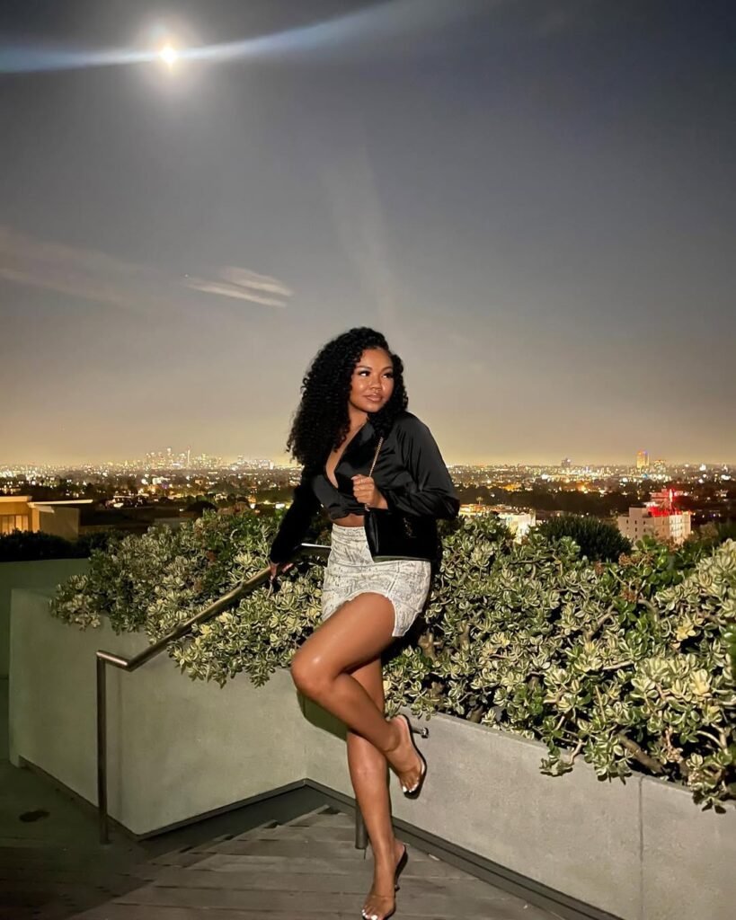 Woman in a black satin blouse and white mini skirt with heels, posing under the moonlight on a rooftop — a glamorous Night Out Outfit.