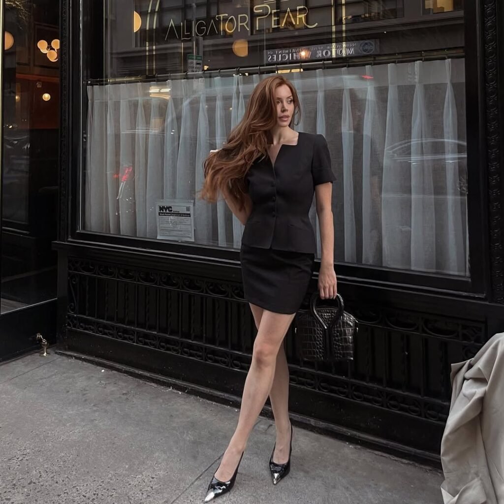 Woman in a sleek black mini skirt suit and pointed-toe heels, posing outside a restaurant — a sophisticated Night Out Outfit.