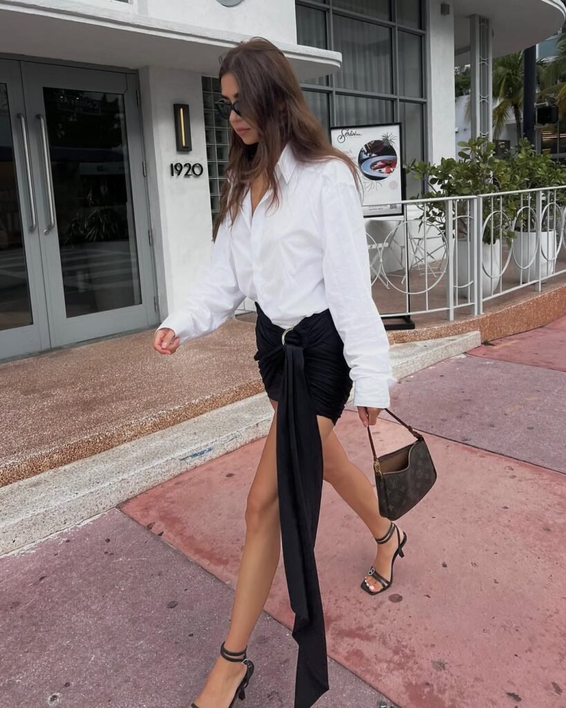 Woman wearing a white button-up shirt and asymmetrical black mini skirt with strappy heels — a sophisticated Night Out Outfit.
