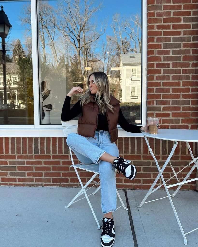 Comfy street-style outfit inspo with a brown puffer vest, black top, and light-wash jeans.