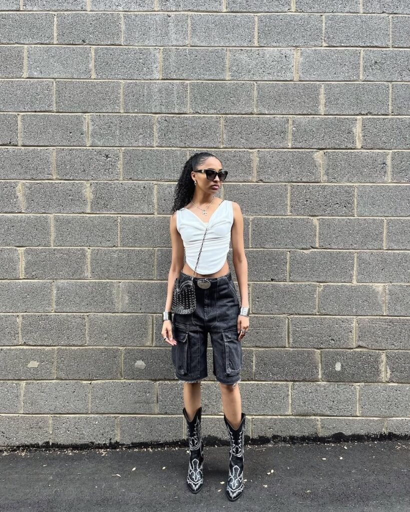 Statement outfit inspo with a ruched white tank and long black shorts paired with cowboy boots.