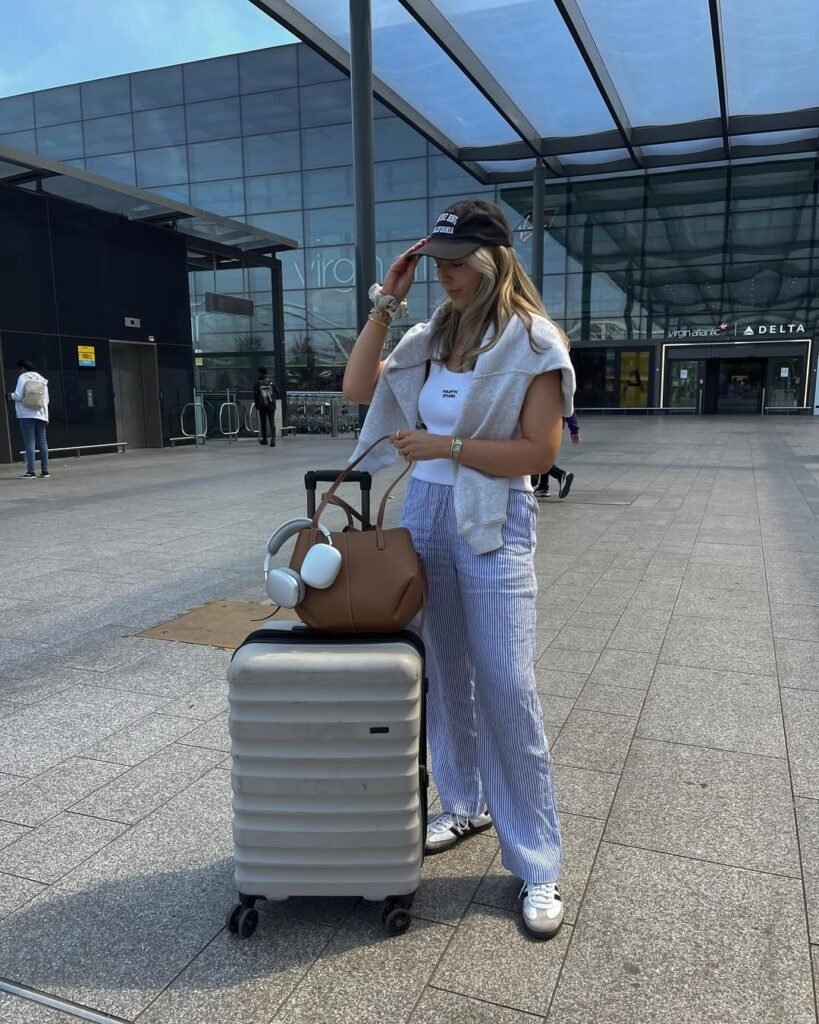 Blue-striped wide pants with a white tank and cap – relaxed and summery airport outfit perfect for warm weather.