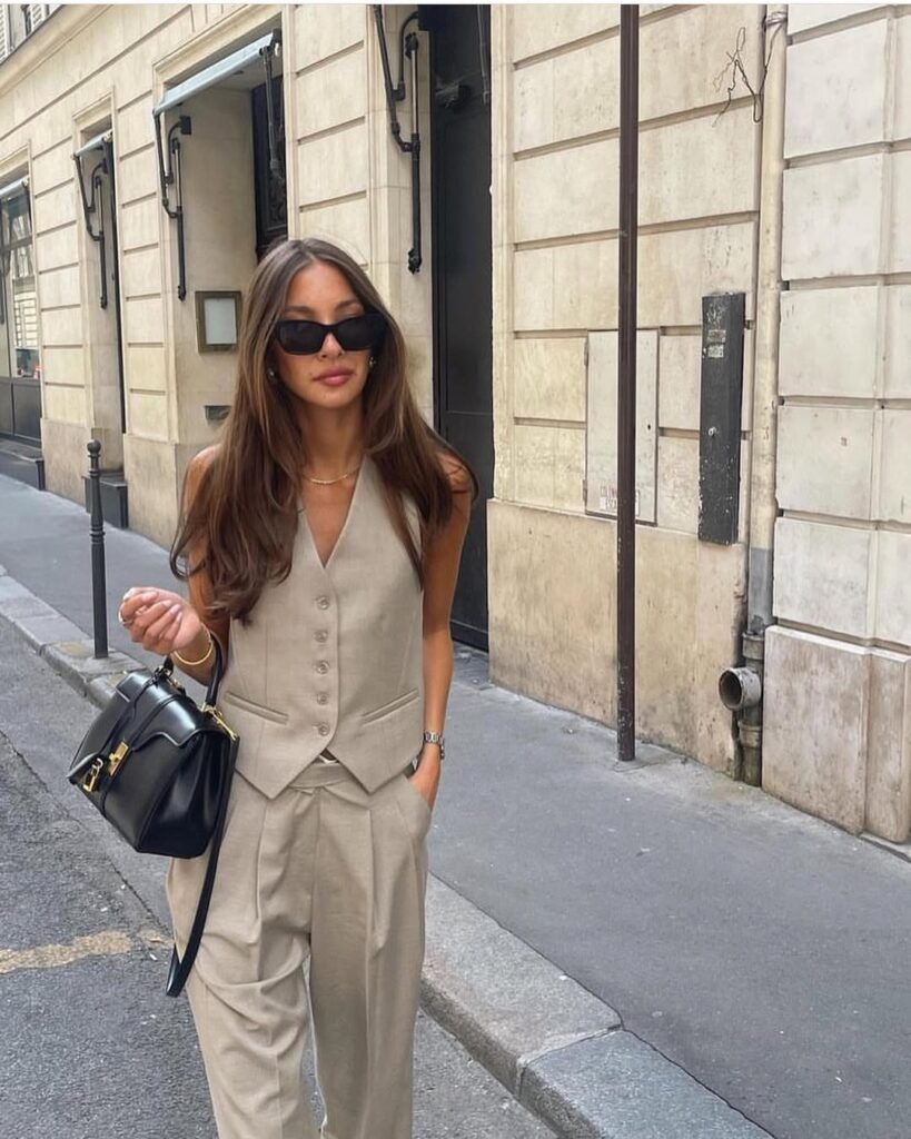 Woman wearing a beige vest and trousers styled with a black handbag and sunglasses – elegant outfit for city strolls.