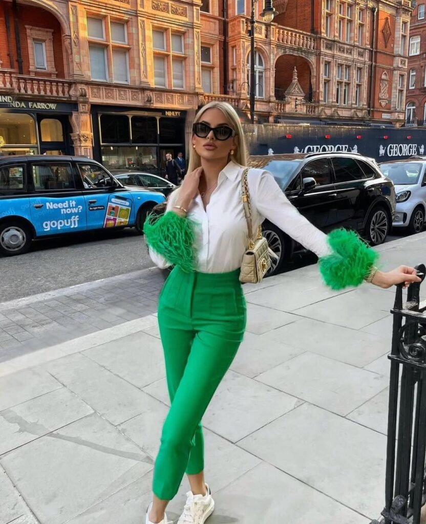 Bold and elegant outfit with green pants, white blouse with green feather cuffs, and a gold handbag – perfect for standing out in the city.