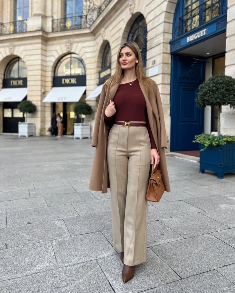 Woman in a maroon top and beige wide-leg trousers, layered with a camel coat – an elegant outfit suited for fall street style.