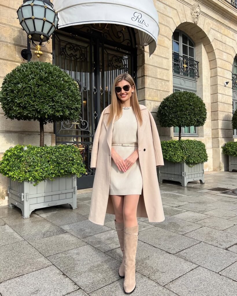 Woman in a cream mini dress with a matching coat and knee-high boots – cozy yet elegant outfit for cool-weather chic.