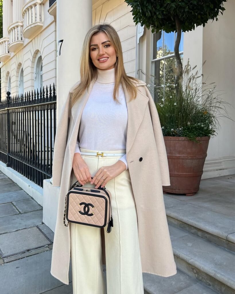 Chic woman in a cream coat, white turtleneck, and wide-leg pants holding a Chanel bag – elegant outfit idea for winter.