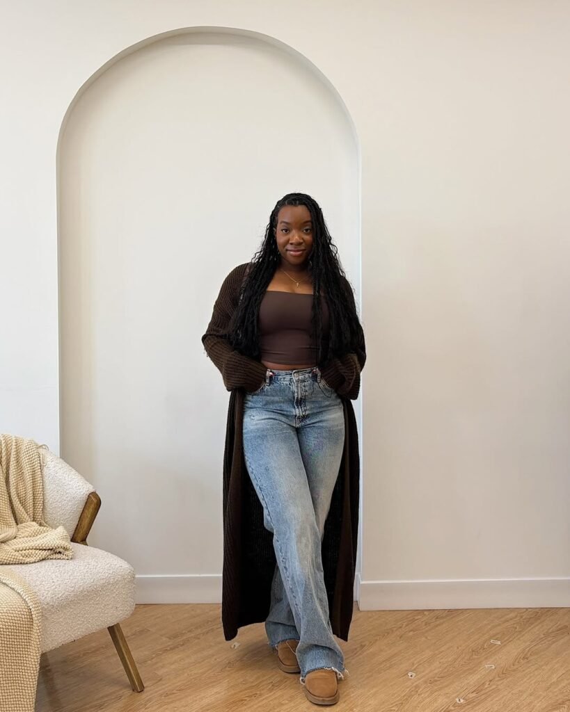 Woman wearing a long dark brown cardigan outfit with a crop top and light wash jeans.