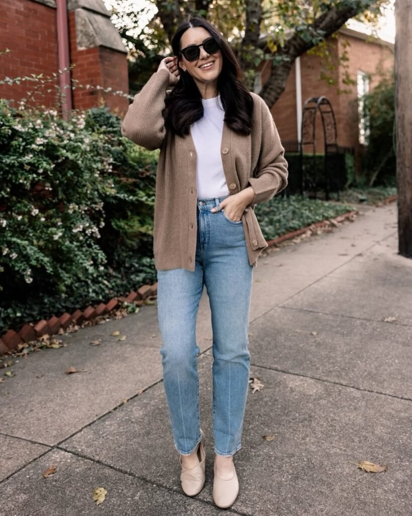 Woman in a beige cardigan outfit with white tee and blue jeans on a sidewalk.