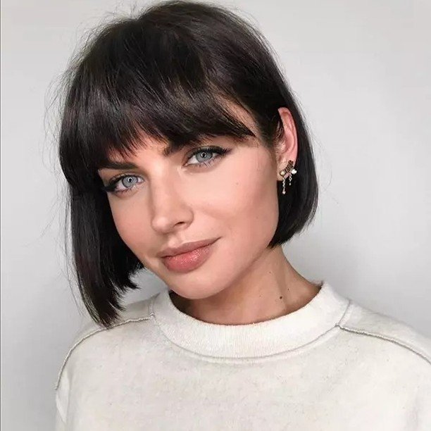 Woman with a sleek black bob and bangs, showcasing cute hairstyles for short hair.