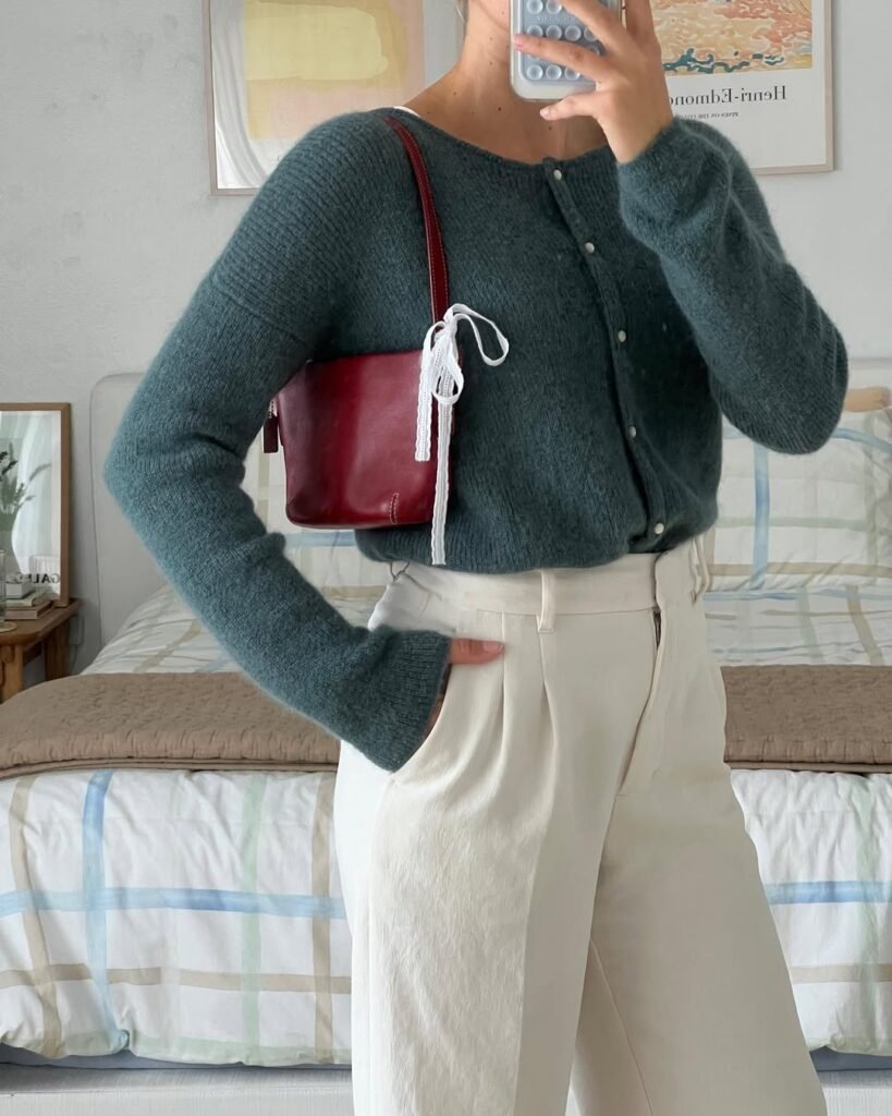 Chic cardigan outfit featuring a dark green cardigan, cream trousers, and a burgundy shoulder bag.