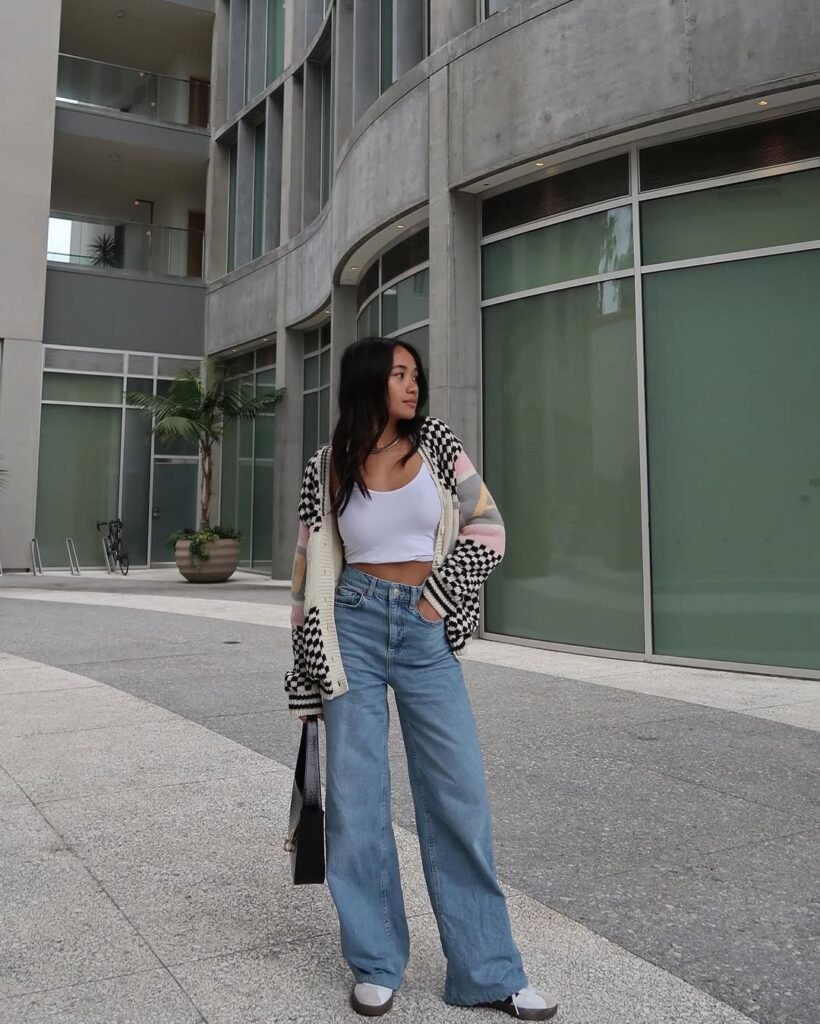 Stylish streetwear cardigan outfit with a checkered and colorful knit cardigan, white crop top, and wide-leg jeans.
