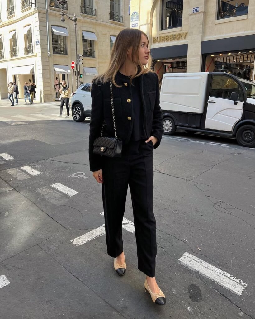 Elegant black cardigan outfit with a matching top and pants, accessorized with a quilted handbag in a city setting.