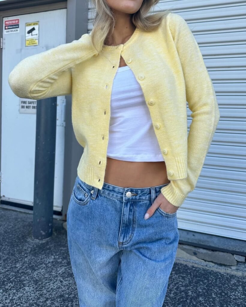 Casual yellow cardigan outfit worn with a white crop top and baggy jeans.