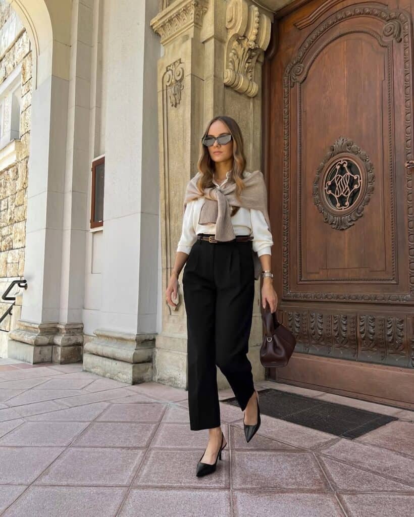 Woman wearing black trousers and white blouse near a grand wooden door – old money outfits inspired by classic European style.