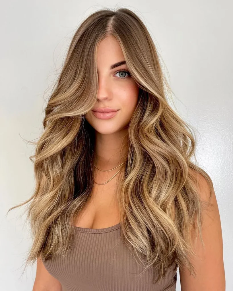 A young woman with voluminous, light brown hair styled in soft waves, showcasing a beautiful, sun-kissed brown hair color idea.