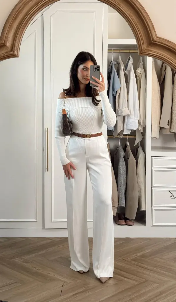  Woman wearing an all-white stylish work outfit with off-shoulder top and high-waisted trousers.