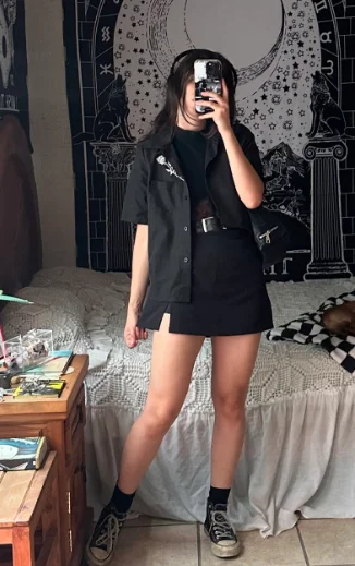 Grunge Outfits: Person wearing black short-sleeve shirt over a black mini skirt with belt and black socks and sneakers, taking a mirror selfie in a room.