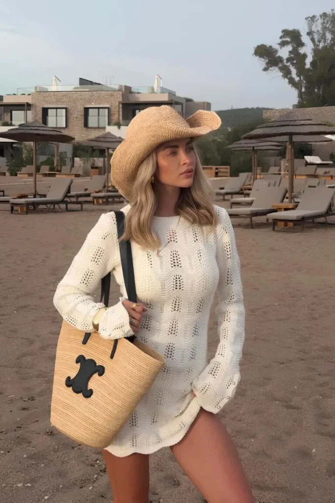 Woman on the beach wearing a white crochet cover-up dress, straw hat, and tote bag — cozy and stylish for outfit ideas summer.