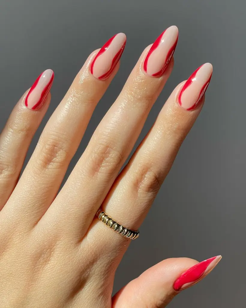 Red Nail Ideas featuring nude nails with abstract red swirls, paired with a gold ring.