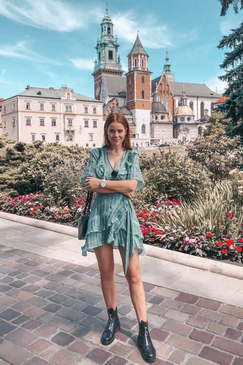A woman in a green ruffled wrap dress and black ankle boots posing in front of a historic cathedral, showcasing a playful yet chic European summer outfit.