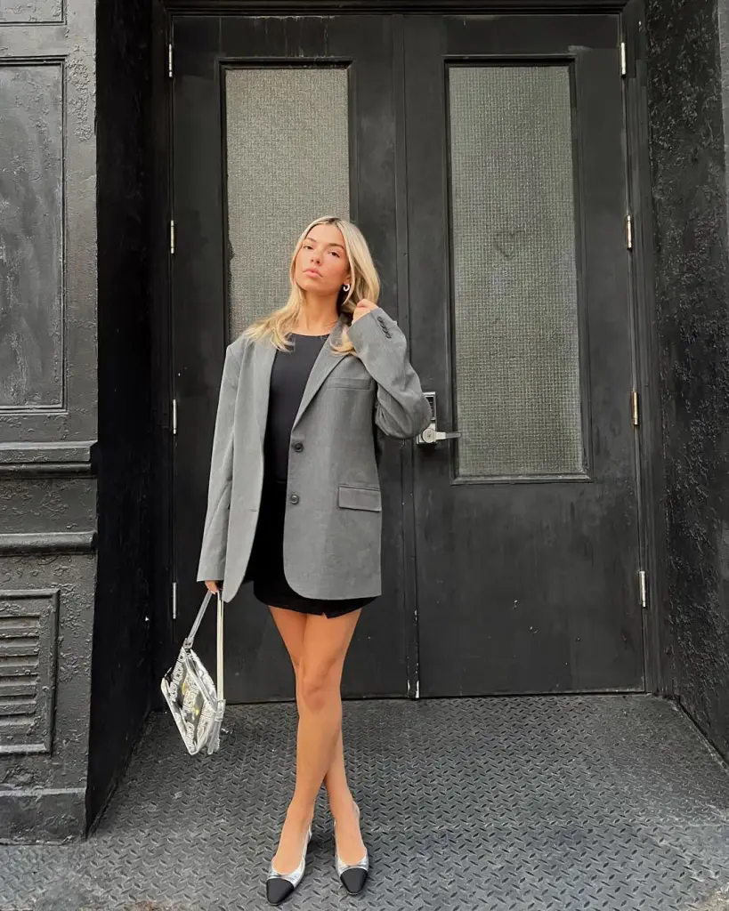 Sophisticated classy outfit with a little black dress layered under an oversized gray blazer, paired with pointed heels and a patterned handbag for a polished city chic vibe.