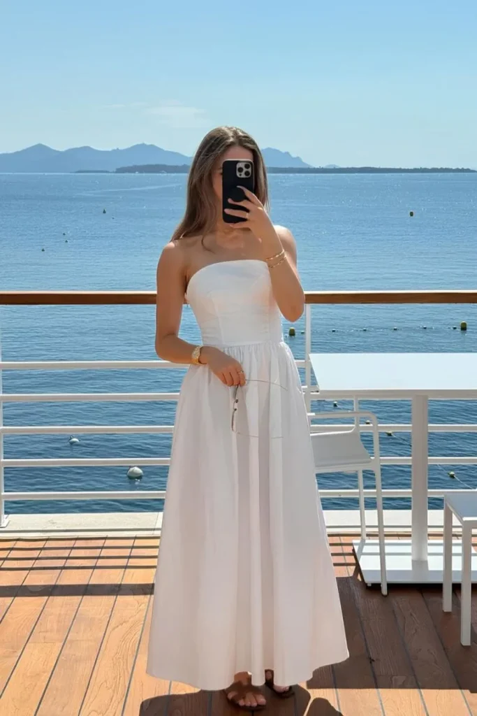 Elegant look featuring a strapless white maxi dress with a scenic seaside backdrop — minimal and classy outfit ideas summer.