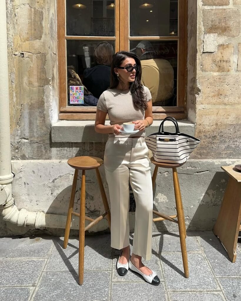  Woman in a beige knit top and cropped cream trousers, paired with two-tone loafers and statement sunglasses — a relaxed and stylish work outfit perfect for a coffee break.