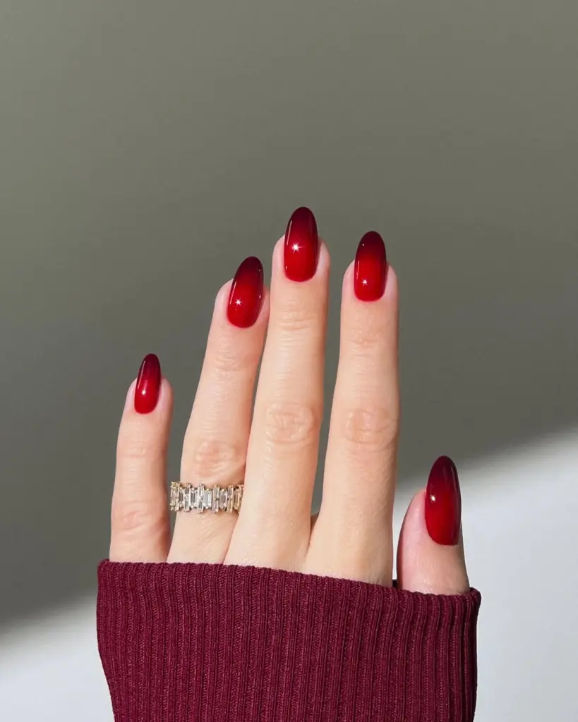 Red Nail Ideas showing a deep red to black ombre effect on almond-shaped nails, accessorized with a gold statement ring.