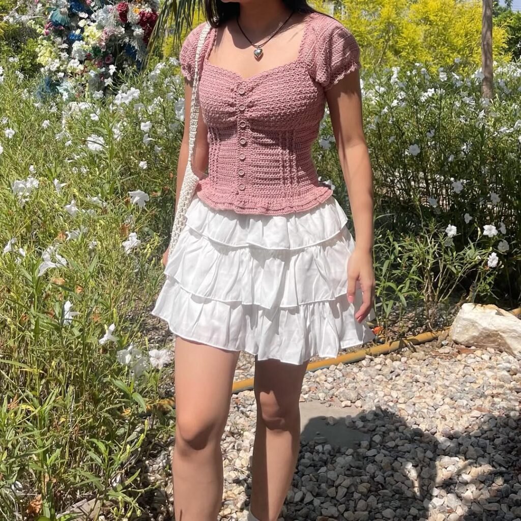 Woman wearing a mauve crochet button-up top with puff sleeves, styled with a tiered white ruffle skirt – Crochet Outfits.