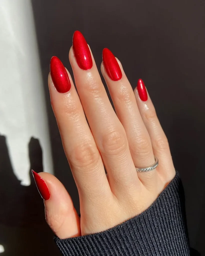 Red Nail Ideas highlighting shiny metallic red almond nails with a silver ring, set against a cozy black sweater.