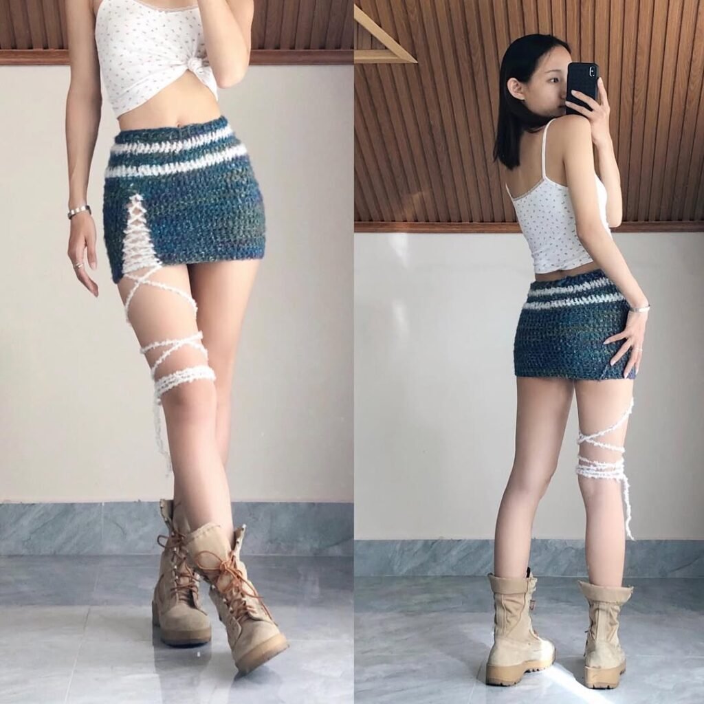 Woman wearing a blue and green striped crochet mini skirt with white crisscross thigh ties, styled with a white crop top and boots – Crochet Outfits.