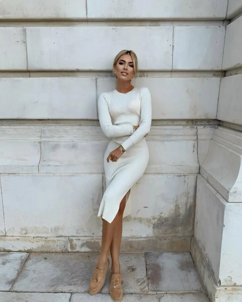 Classy outfit featuring a fitted ivory knit dress with long sleeves and a side slit, paired with tan loafers and gold accessories for an effortlessly elegant street-style look.