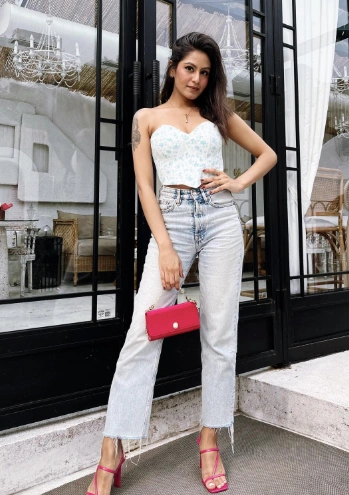 A woman in a white floral corset top and ripped denim jeans with pink heels, carrying a small pink handbag, exuding a youthful and trendy aura, perfect for a brunch date.