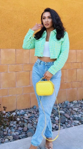 A woman dressed in a mint green cropped jacket and light blue jeans with a yellow handbag, radiating casual chic vibes, perfect for a relaxed yet fashionable brunch look.