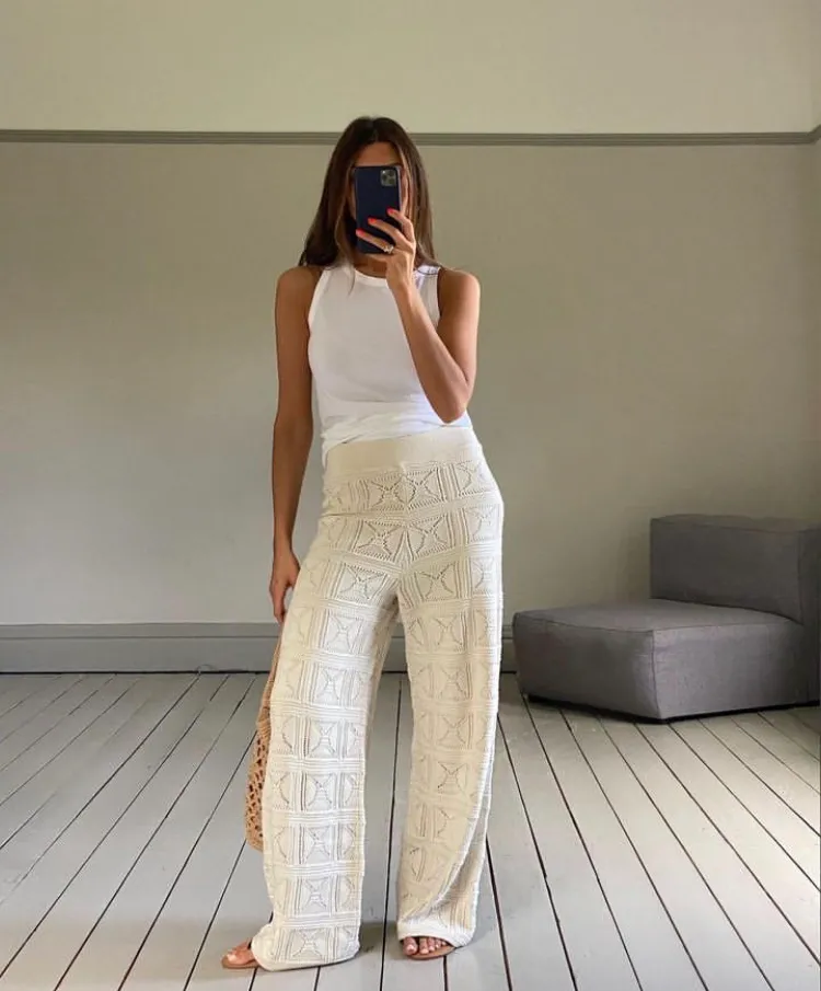 Woman in a sleeveless white top paired with cream-colored wide-leg crochet pants, posing indoors – Crochet Outfits.