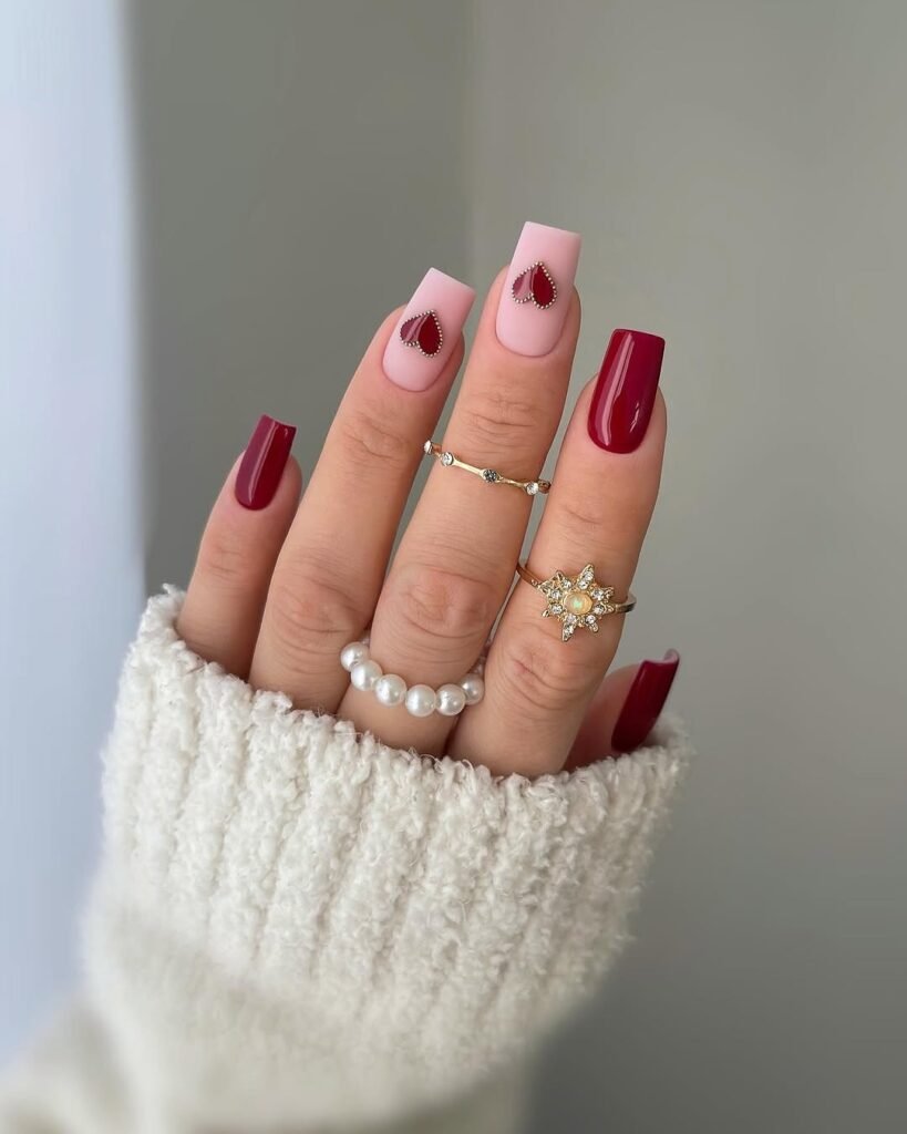 Red Nail Ideas featuring pale pink nails with red heart designs and gold rings with pearls and gemstones."