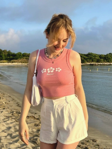 Beachside aesthetic with a pink cropped tank top with floral design and white high-waisted shorts — sweet and breezy outfit ideas summer.