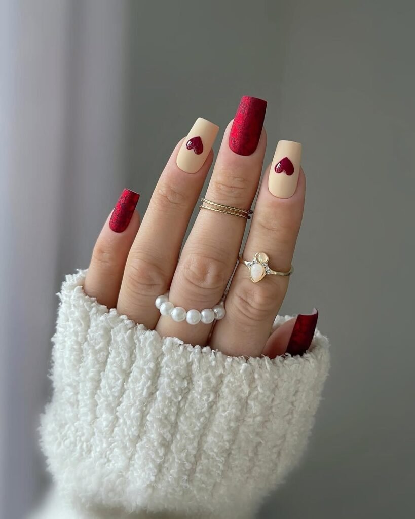 Red Nail Ideas with a mix of red solid, white nails with red hearts, and burgundy nails with rhinestone borders, paired with gold rings.