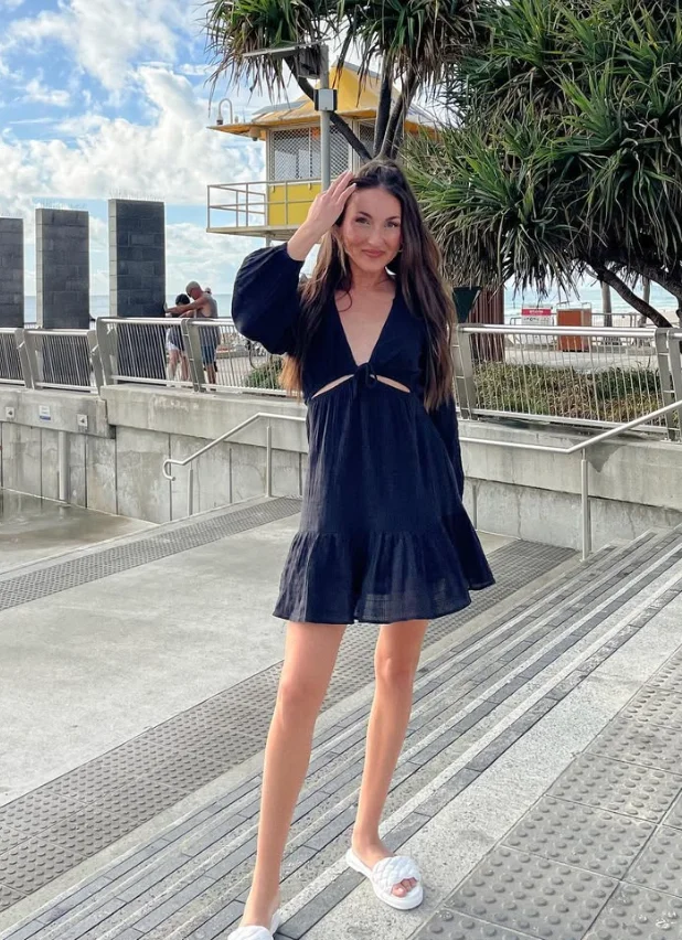 Beach outfit featuring a black mini dress with puffed sleeves and front cut-out detail, worn with white slippers for a casual seaside stroll.