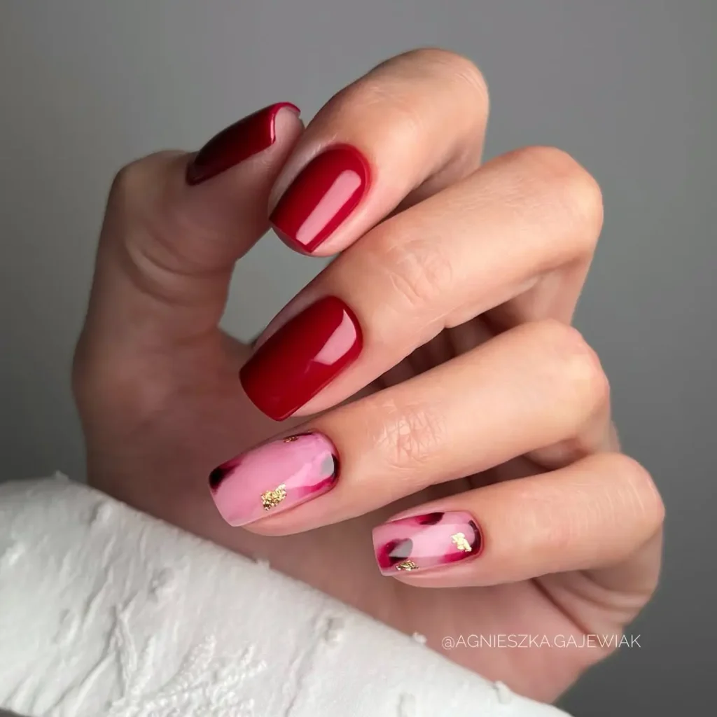 A hand with square-shaped nails painted glossy red, with two accent nails in pink featuring red and gold abstract designs, perfect Red Nail Ideas inspiration.
