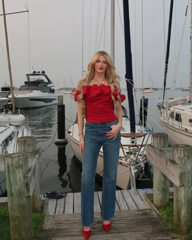 Elegant red off-shoulder ruffle top paired with straight-leg jeans and red pointed heels, a classy outfit for a dockside dinner date.