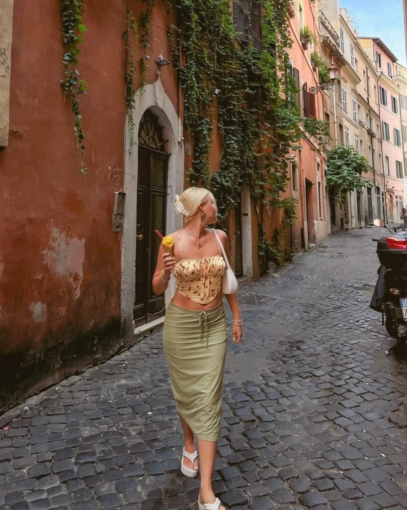 A woman walking on a cobbled street in Rome, wearing a green skirt and floral corset top while holding gelato — a playful and chic European summer outfit.