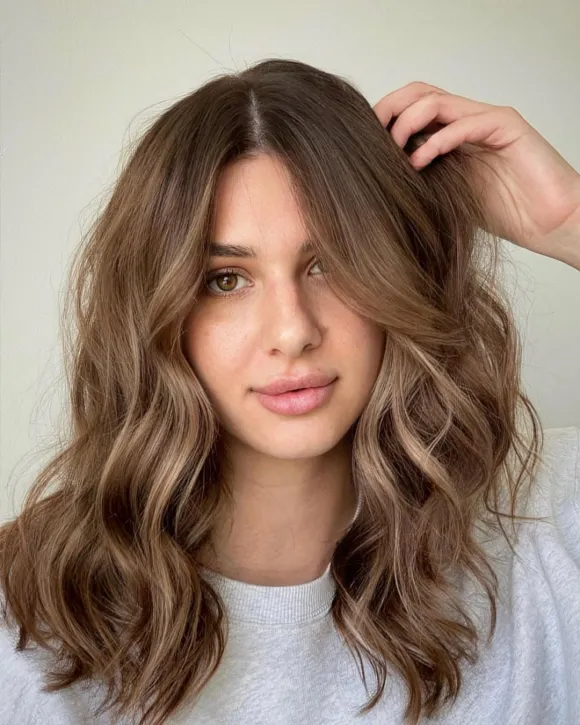 A woman with medium brown hair styled in loose, bouncy waves, demonstrating a rich, warm brown hair color idea.
